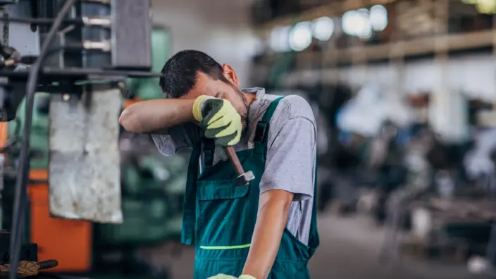 Azubi im Handwerk hält sich vor Stress die Hand vors Gesicht. 