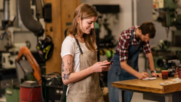 Junge Auszubildene steht in der Werkstatt und schaut auf ihr Handy.