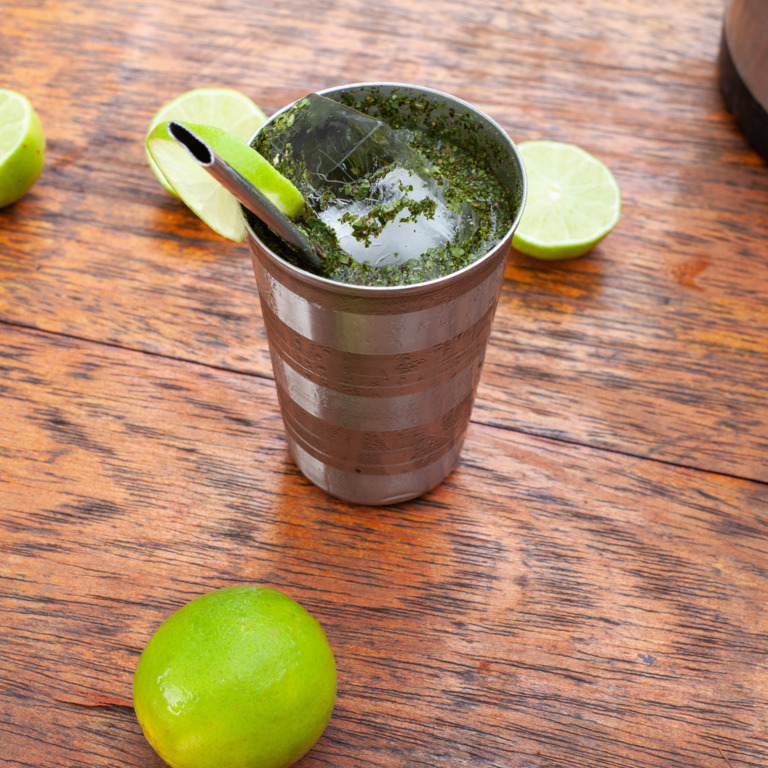 Ein Becher mit Maté-Tee, Eiswürfeln und Limetten.