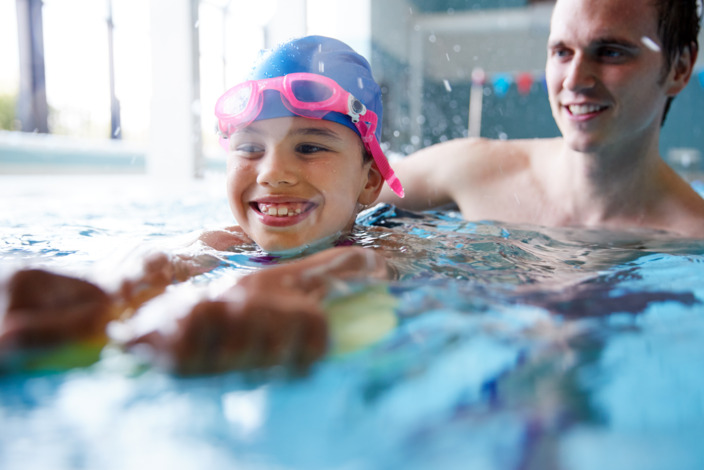 Kind lernt mit Vater schwimmen in der Schwimmhalle