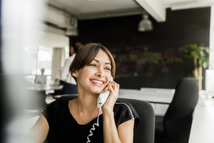 Mitarbeiterin sitzt im Büro und führt ein Kundengespräch am Telefon