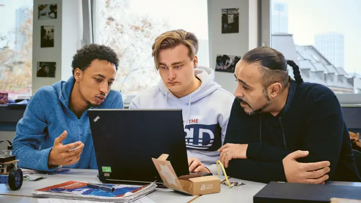 Zwei Auszubildene sitzen mit ihrem Lehrer zusammen am Laptop.
