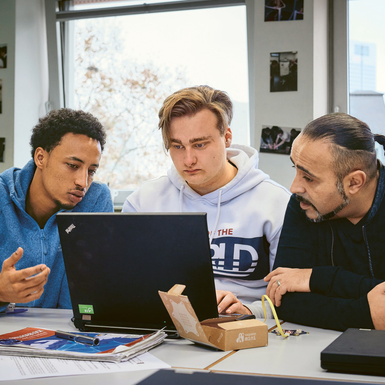 Drei Männer unterschiedlicher Herkunft sitzen an einem Schreibtisch