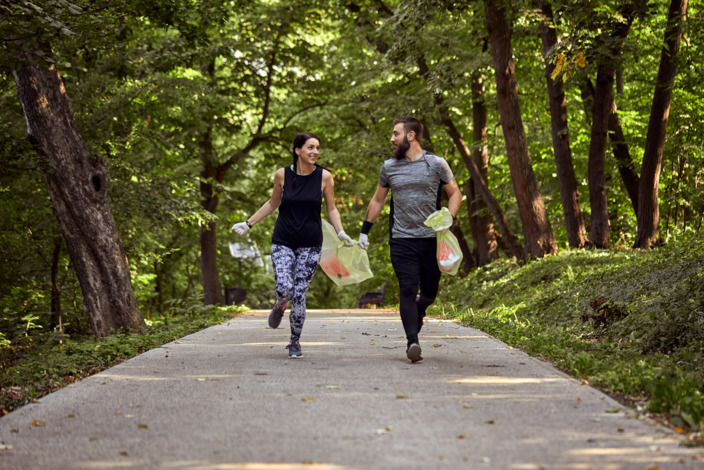 Mann und Frau joggen durch den Wald und sammeln Müll