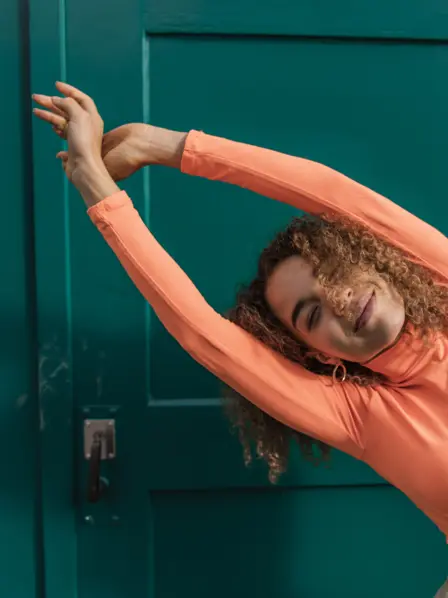 Frau in orangenem Sweatshirt dehnt ihren Oberkörper, um zu entspannen.