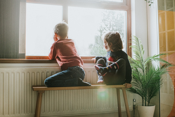 Kinder sitzen in Wohnung an der Heizung und schauen aus dem Fenster