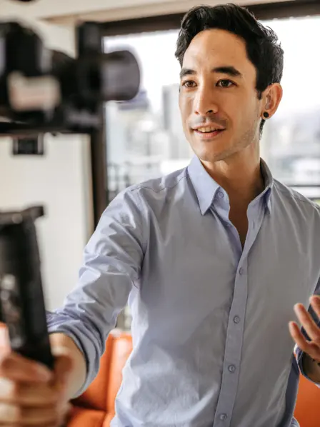 Männlicher Influencer hält Gimbal mit Kamera in der Hand und filmt sich selbst.