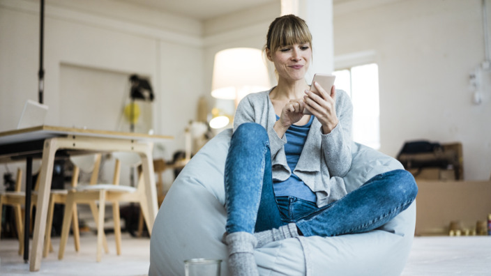 Frau sitzt auf einem Sitzsack und benutzt ihr Smartphone