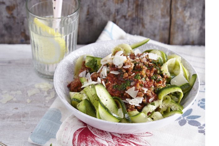 appetitlich in einem tiefen Teller angerichtete Portion Zoodles und ein Glas mit selbstgemachter Zitronenlimonade